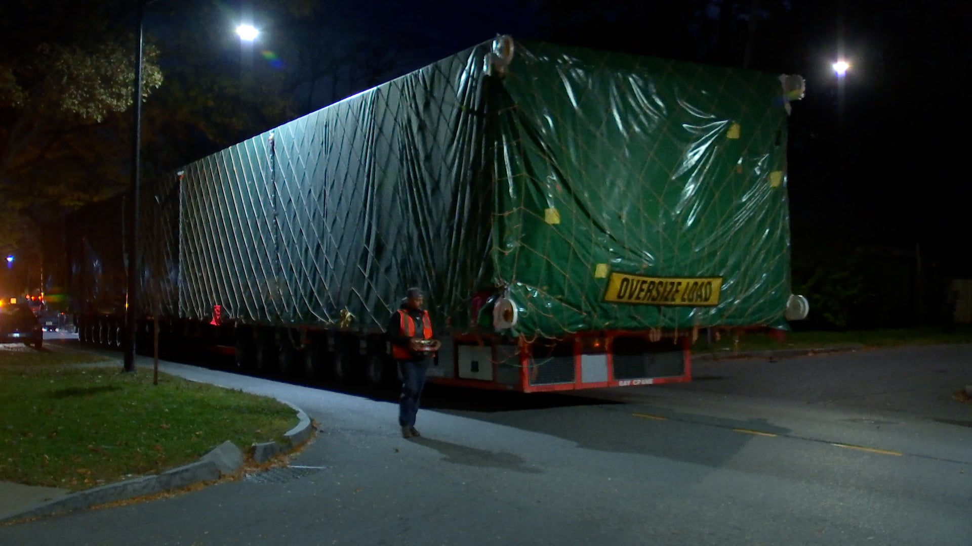Massive industrial tanks being transported through a city at night, escorted by police.